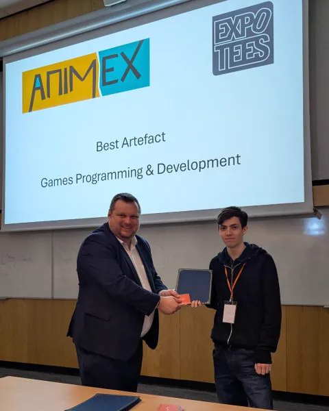 Oliver Neal collecting the Best Artefact award for Games Programming and Development at ExpoTees 2026, in front of a screen reading Best Artefact, Games Programming & Development